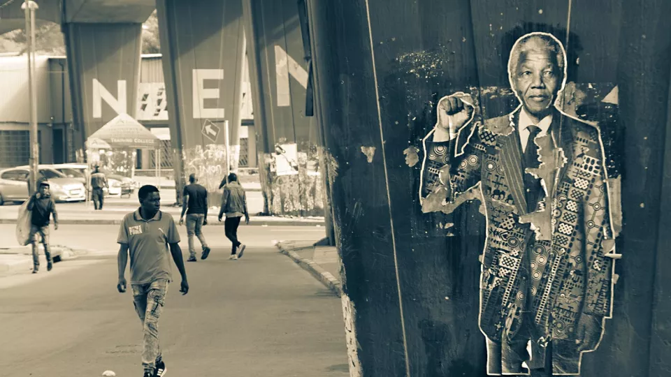 Gatukonst föreställande Nelson Mandela. I bakgrunden personer som går på en gata i Sydafrika. Svartvitt foto.