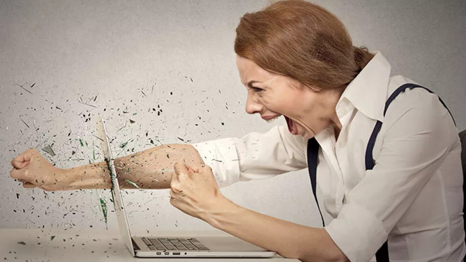 En kvinna slår knytnäven igenom skärmen på en laptop. Hon ser arg ut. Foto.