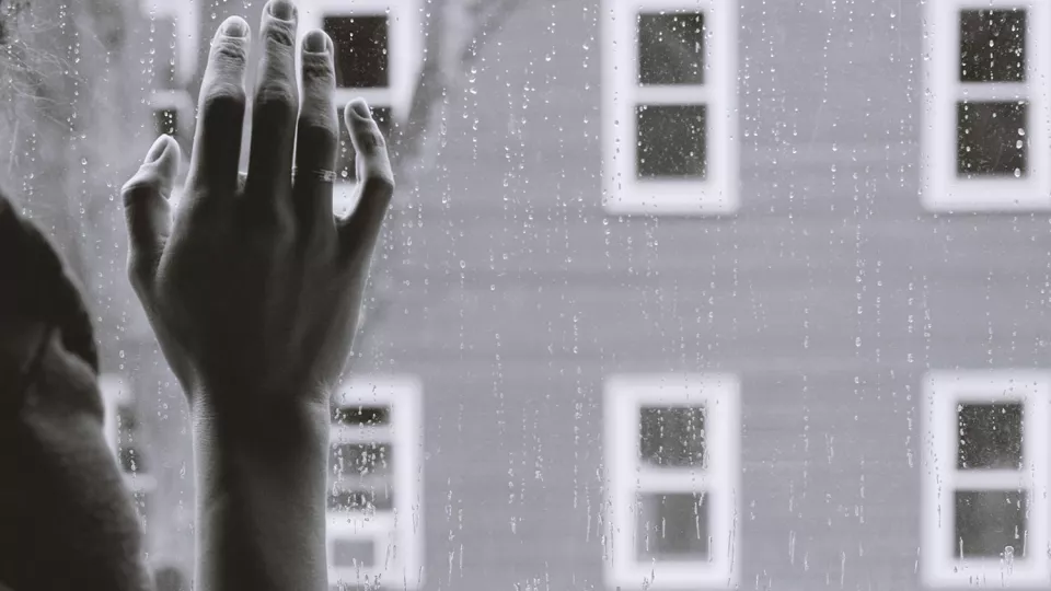 En hand mot ett fönster där regndroppar fastnat. Utsikt mot fönster. Foto.