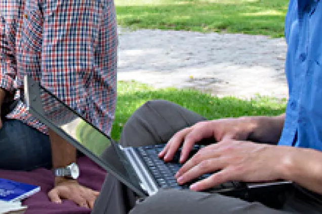 Händer vid en laptop i gröngräset. Foto.