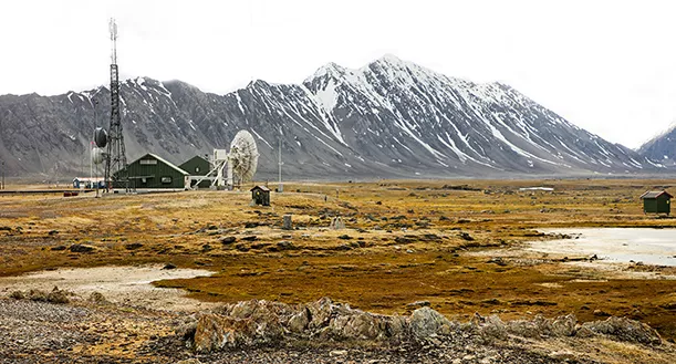 Platt, brunt arktiskt landskap med snötäckta berg i bakgrunden